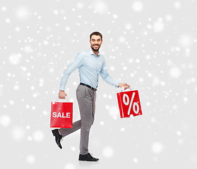 Image showing smiling man with red shopping bags over snow