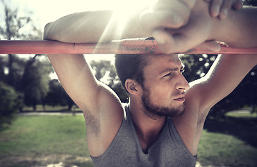 Image showing young man exercising on horizontal bar outdoors