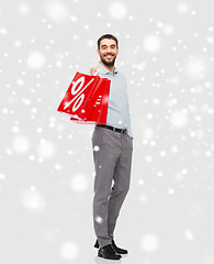 Image showing smiling man with red shopping bag over snow