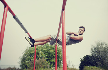 Image showing young man doing sit up on parallel bars outdoors