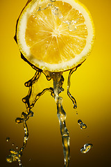 Image showing Lemon juice pouring down from half of  isolated on orange background