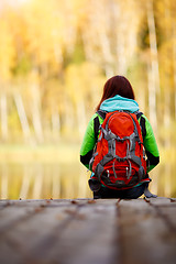 Image showing Brunette sitting back with backpack on bridge near water