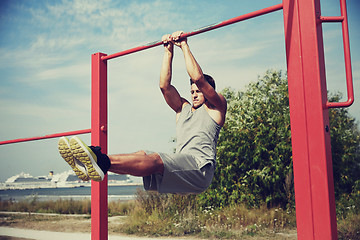 Image showing young man exercising on horizontal bar outdoors