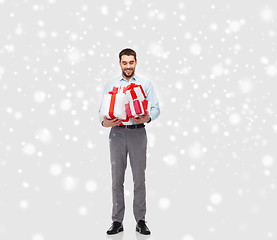 Image showing happy young man holding christmas gifts over snow