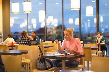 Image showing Young woman eating pizza at airport restaurant while waiting for flight departure.