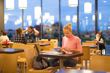 Image showing Young woman eating pizza at airport restaurant while waiting for flight departure.