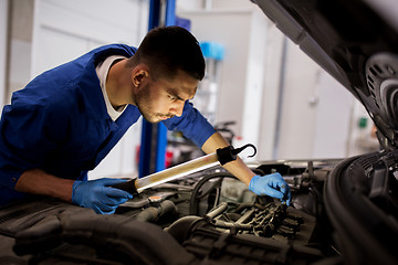 Image showing mechanic man with lamp repairing car at workshop