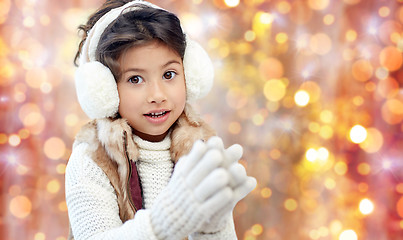 Image showing happy little girl in earmuffs over holidays lights