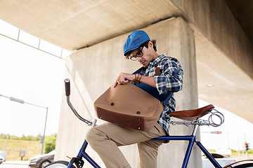 Image showing hipster man with bicycle looking something in bag