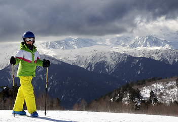 Image showing Young skier with ski poles in sun mountains and cloudy gray sky