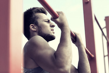 Image showing young man exercising on horizontal bar outdoors