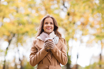 Image showing happy young woman drinking coffee in autumn park