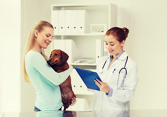 Image showing happy woman with dog and doctor at vet clinic