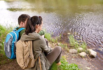 Image showing couple with backpacks sitting on river bank