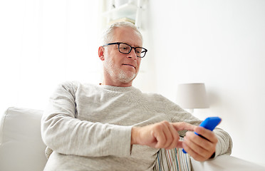 Image showing happy senior man texting on smartphone at home