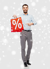 Image showing smiling man with red shopping bag over snow