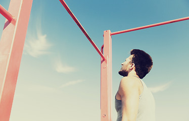 Image showing young man exercising on horizontal bar outdoors