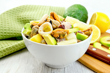 Image showing Salad with seafood and lemon in bowl on light board