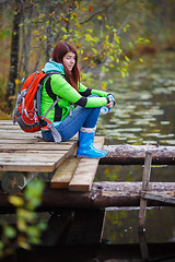 Image showing Young brunette with travel backpack sits on bridge by pond