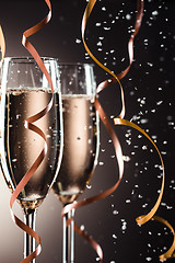 Image showing Two champagne glasses, decorative ribbon on dark background with snowfall