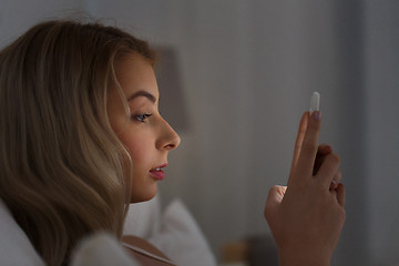 Image showing young woman with smartphone in bed at night