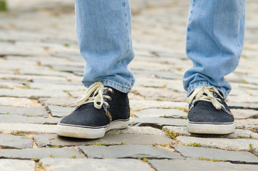 Image showing Feet dressed in blue jeans and sneakers man closeup on stone pavement