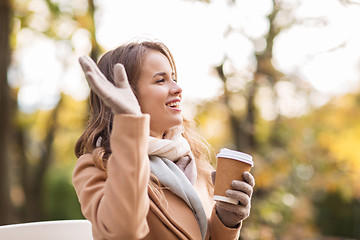 Image showing happy young woman drinking coffee in autumn park