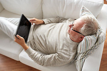 Image showing senior man with tablet pc lying on sofa at home