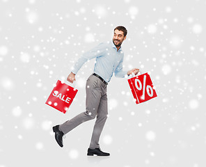 Image showing smiling man with red shopping bags over snow