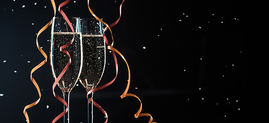 Image showing Glasses of champagne decorated ribbons on black background with snowflakes