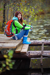 Image showing Smiling brunette with travel backpack sits by pond in woods