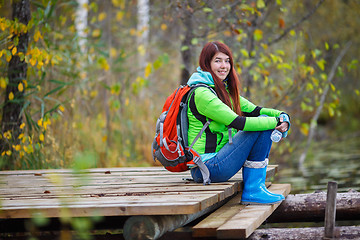 Image showing Brunette with long hair and backpack tourist sits on bridge