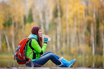 Image showing Girl with long hair drinking water sitting among autumn trees