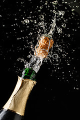 Image showing Champagne cork popping and splashing on black background