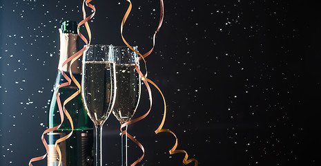 Image showing Two champagne glasses and bottle on dark background with snowfall