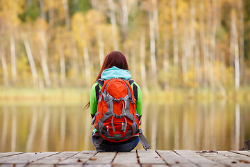 Image showing Girls with backpack sitting back on wooden bridge