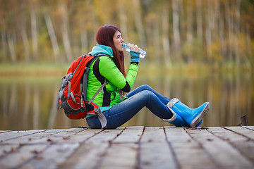 Image showing Brunette drinks water sitting in autumn trees