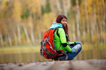 Image showing Girl with backpack sitting on bridge at lake