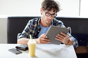 Image showing man with tablet pc and earphones sitting at cafe