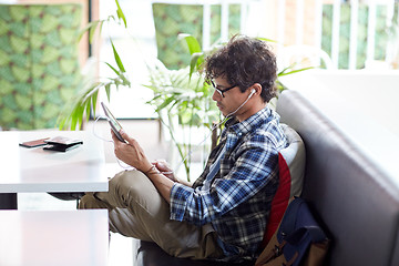 Image showing man with tablet pc and earphones sitting at cafe