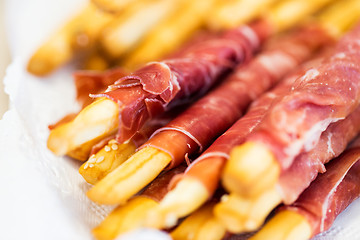 Image showing close up of grissini bread sticks with prosciutto