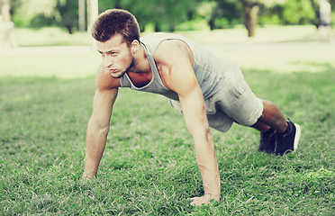 Image showing young man doing push ups on grass in summer park