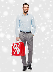 Image showing smiling man with red shopping bag over snow