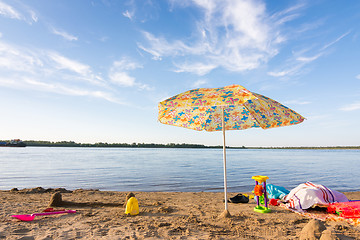 Image showing Parasol on the river bank, under which the scattered items and toys