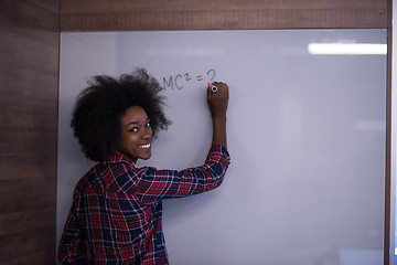 Image showing African American woman writing on a chalkboard in a modern offic