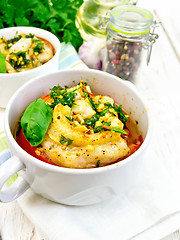 Image showing Fish baked with tomato and garlic in white bowl on board