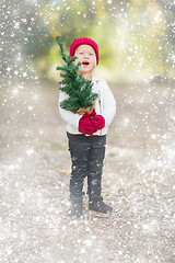 Image showing Baby Girl In Mittens Holding Small Christmas Tree with Snow Effe