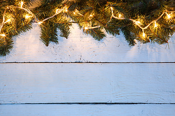 Image showing Christmas wooden background with evergreen branches and golden lighted garland