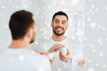 Image showing happy young man applying cream to face at bathroom