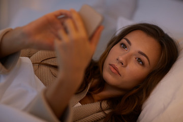 Image showing young woman with smartphone in bed at home bedroom